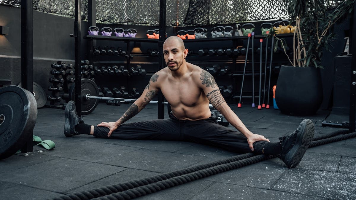 Tattooed man performing a split stretch in a gym, showcasing flexibility and fitness lifestyle in Mexico City.